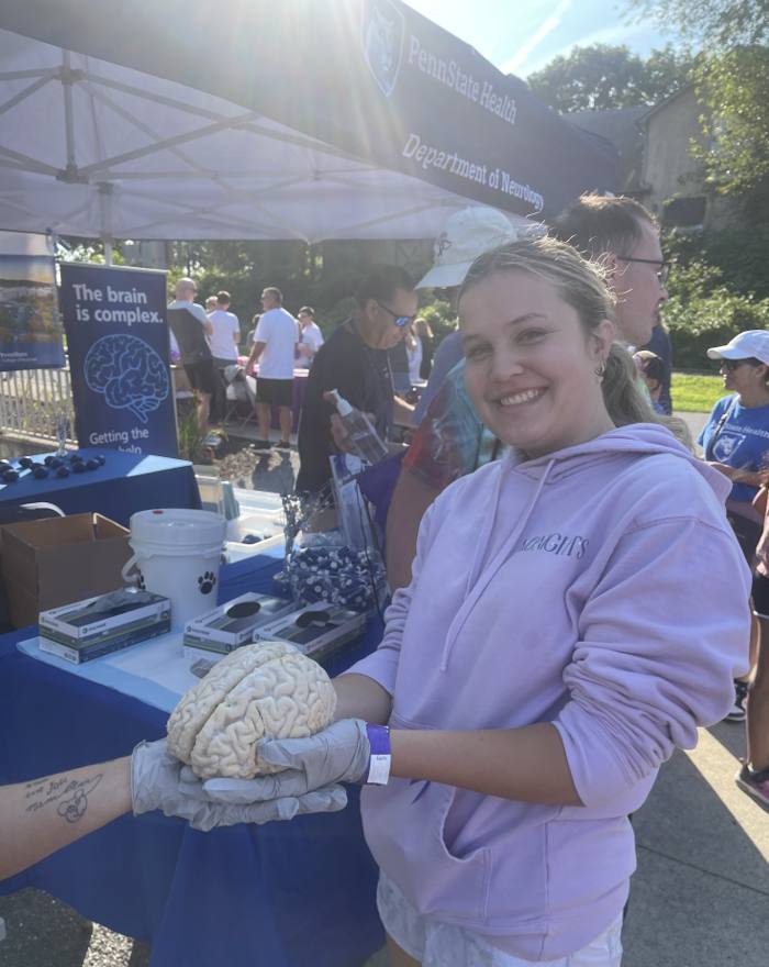 Brooke Shupp, in gloves, holding a preserved human brain at the Penn State Health Department of Neurology table during an EAWCP Epilepsy Walk.